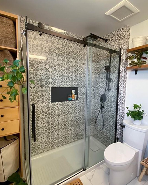 a matte black shower door, with bold black & white patterned shower tiles. bathroom is decorated with multiple plants